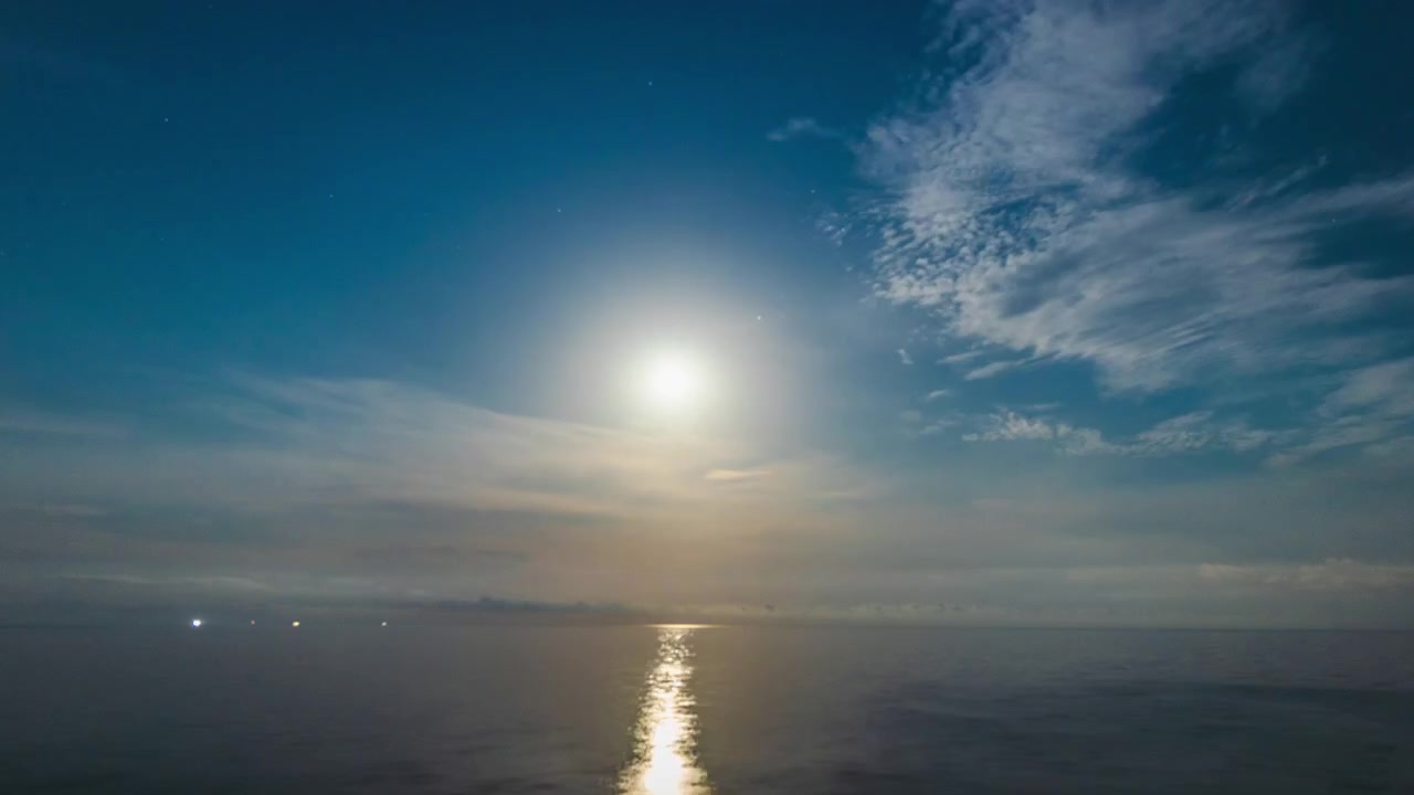 Moonrise over calm Mediterranean Sea during full night timelapse, bright moon ascending through drifting clouds and reflecting shimmering light across water until dawn