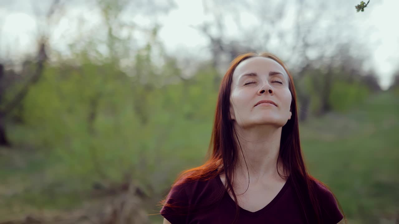 una joven bonita está de pie y relajada en el parque, entre los árboles. movimiento circular de la cámara.