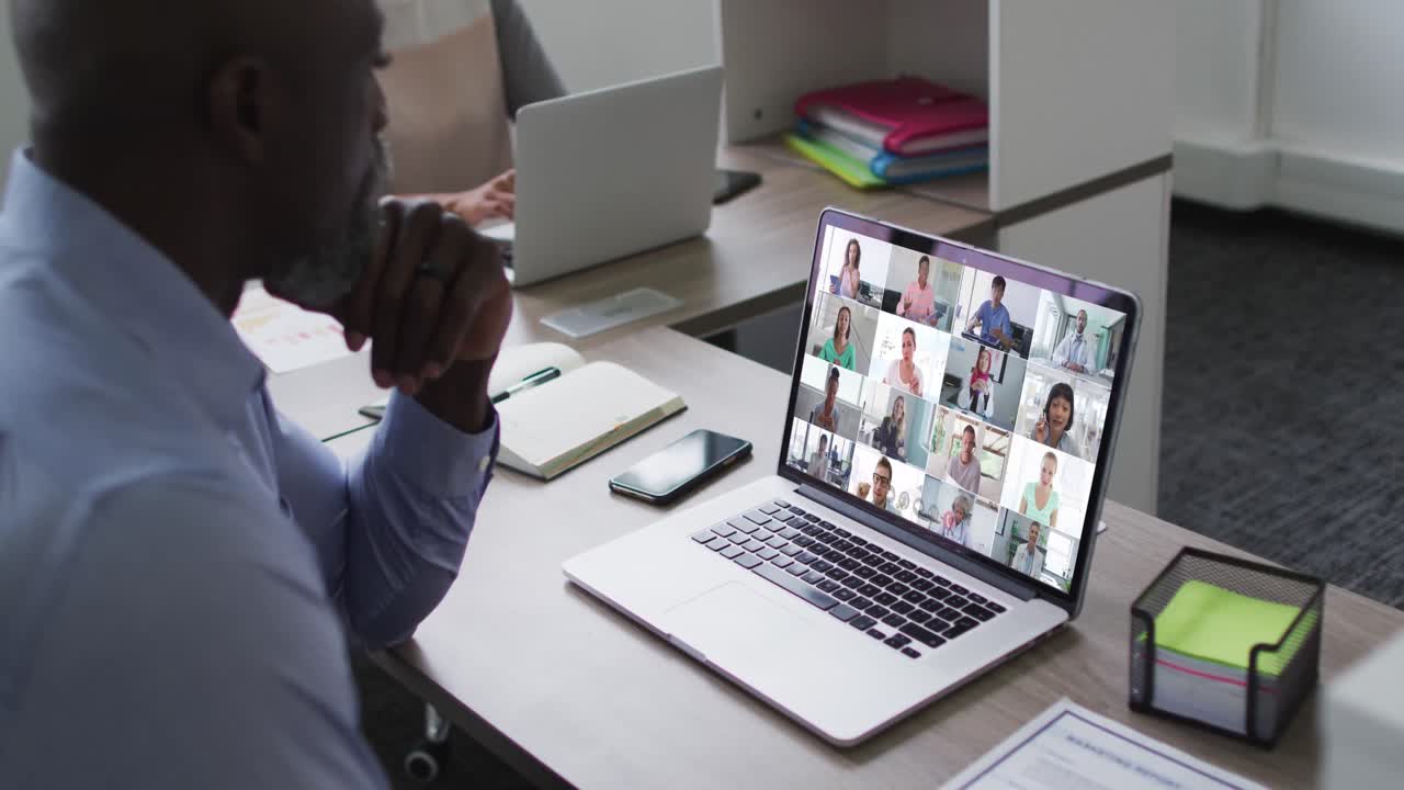 African american senior man having a video conference with colleagues on laptop at office