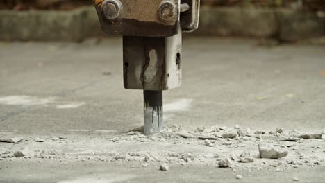 Close-up of excavator hydraulic arm rock breaker working on concrete road with sound