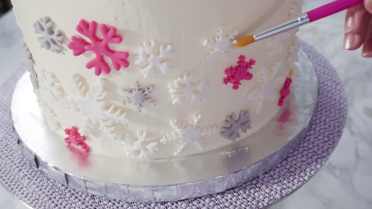 Decorating round funfetti cake with pink and white fondant snowflakes.