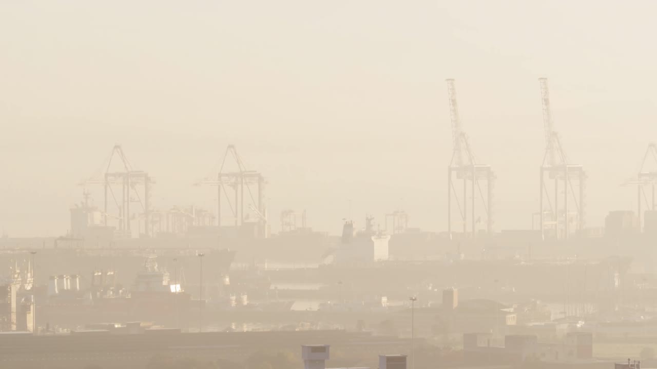 General view of cityscape with multiple buildings and shipyard covered in fog