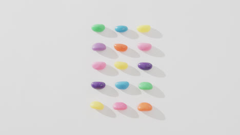 Video-of-overhead-view-of-rows-of-multi-coloured-sweets-with-copy-space-over-white-background