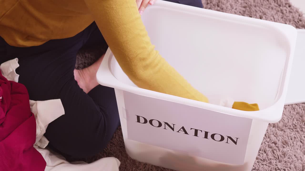 Closu up of woman selecting clothes for donation and putting them in a box