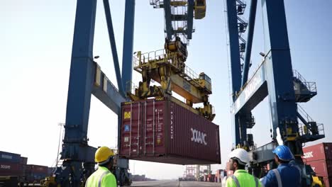 operations at a busy shipping port: crane lifting container for loading onto vessel as workers oversee from below in a dynamic maritime environment