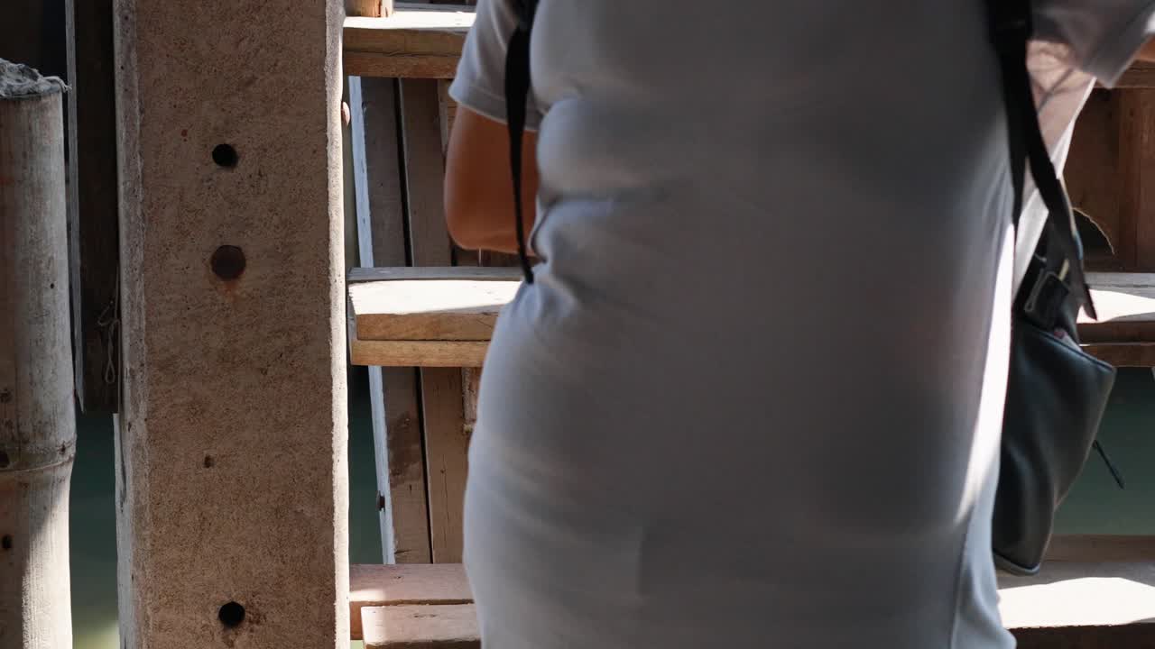 A person climbs wooden stairs at Khlong Lat Mayom Floating Market, Bangkok. Bright daylight enhances the scene's vibrant atmosphere