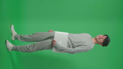 full body of side view asian man holding computer while standing in front of green screen background