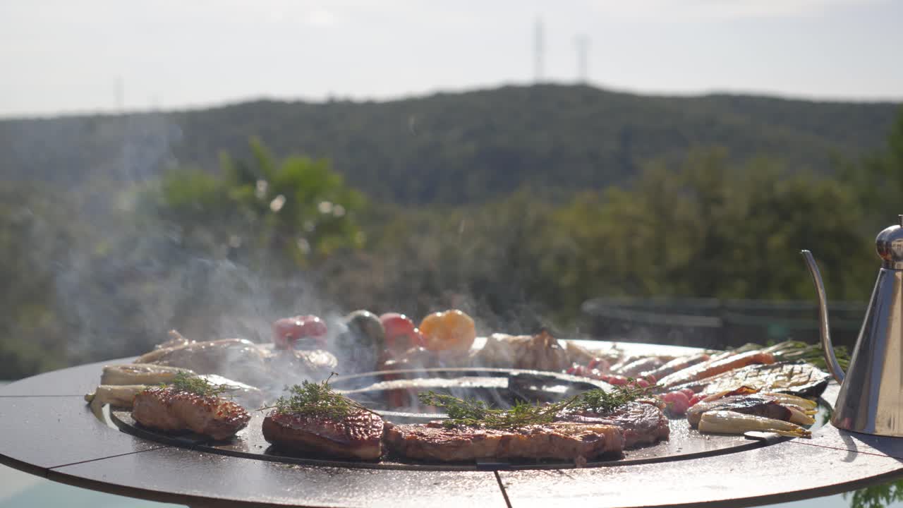 Outdoor barbecue grill with meat and veggies cooking over fire in scenic hillside view