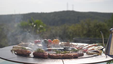 outdoor barbecue grill with meat and veggies cooking over fire in scenic hillside view