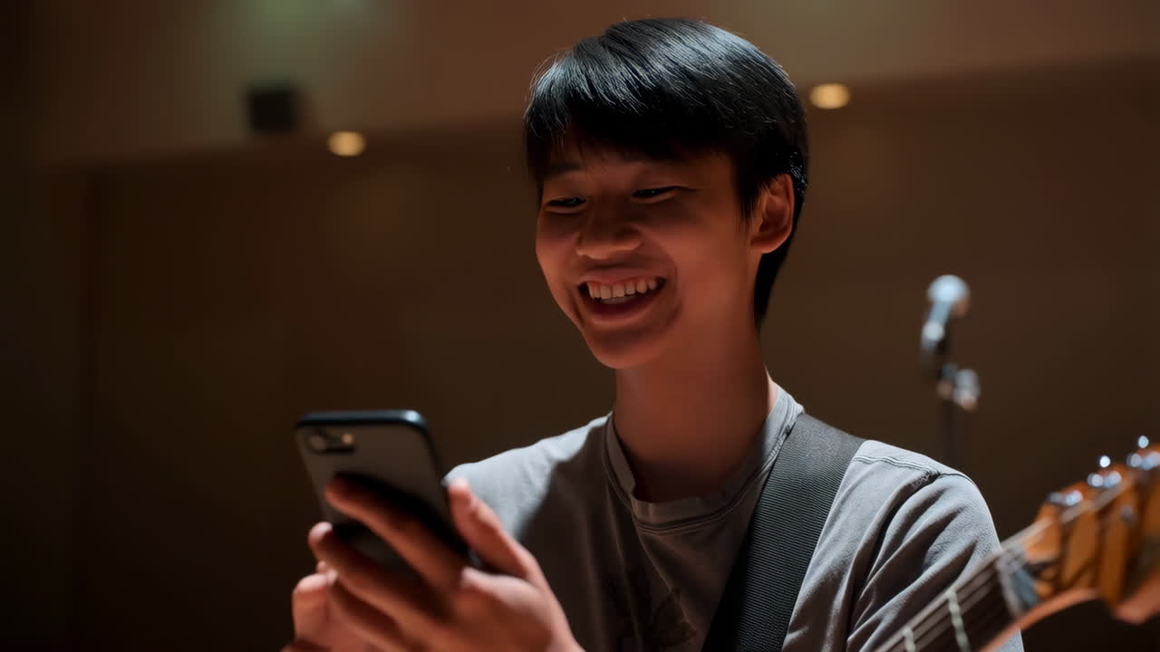 Young man playing guitar and looking at his phone in a music studio