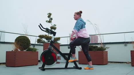 Athletic-woman-riding-on-spinning-stationary-bike-training-routine-on-house-rooftop,-weight-loss