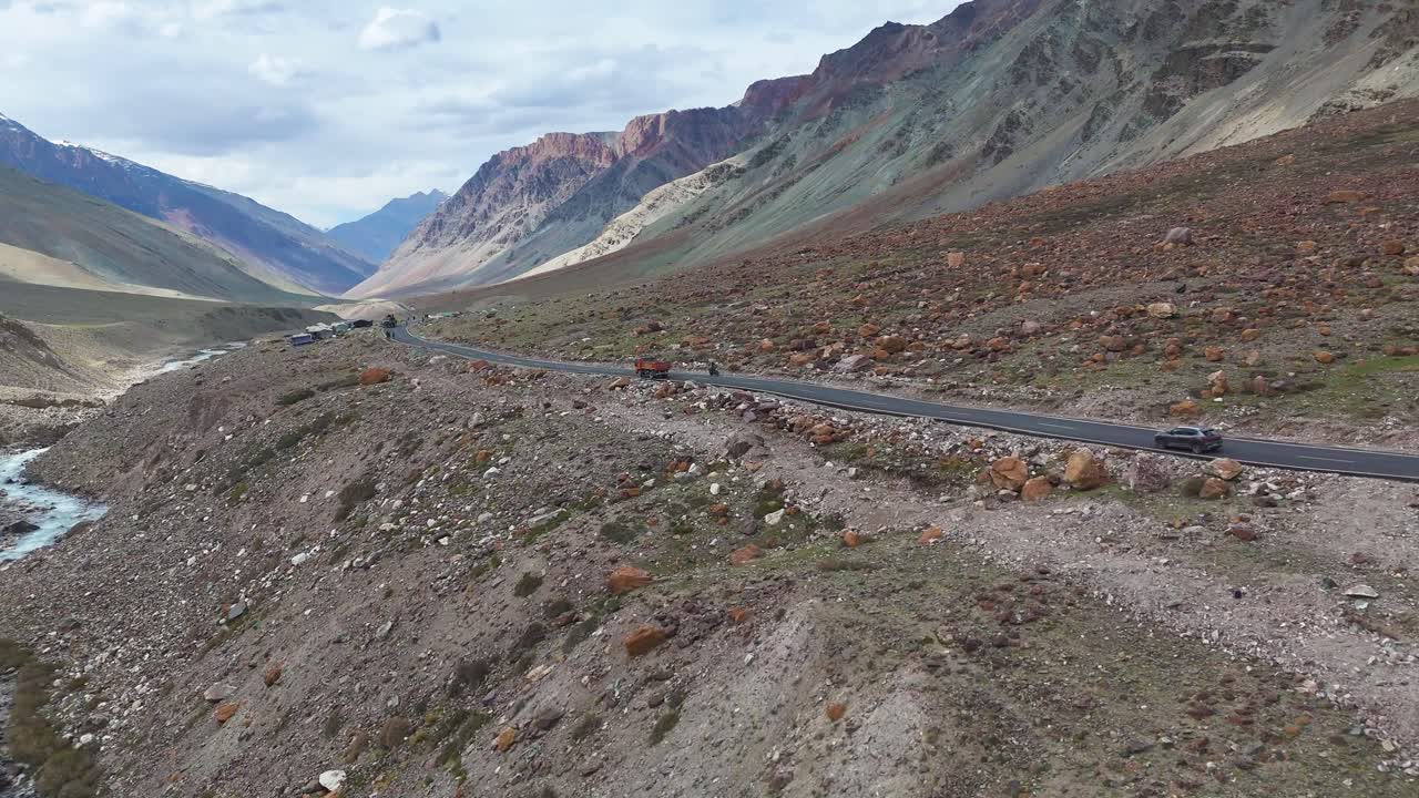Aerial drone shot tracking a vehicle on a straight path with barren mountains on either side in Ladakh.