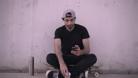 Young Man Relaxing on a Skateboard with Coffee and Phone