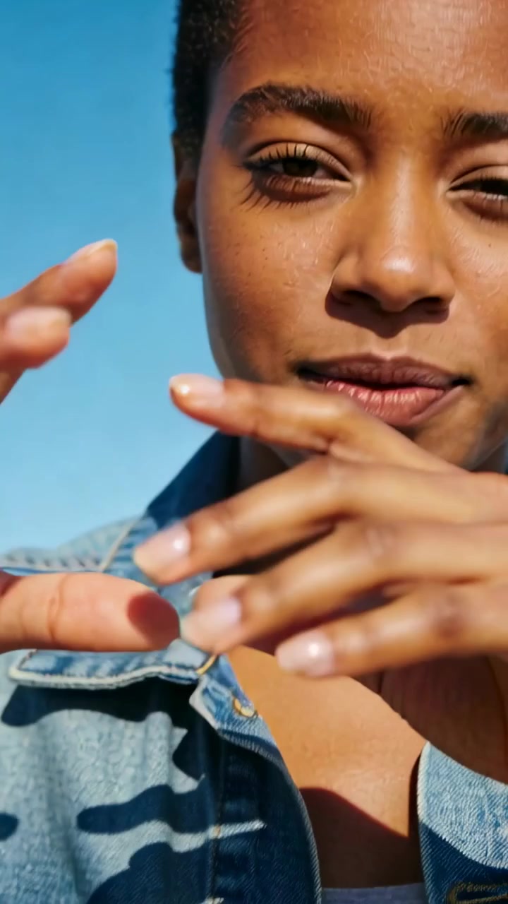 Vertical video: Reaching woman moving fingers to frame lens for camera outdoors, in denim jacket