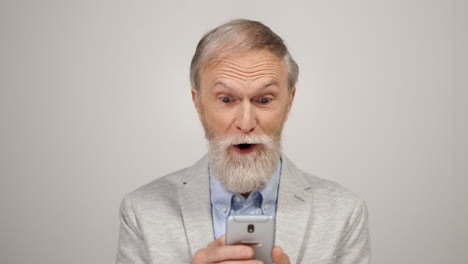 un hombre alegre leyendo noticias por teléfono en el interior. un anciano usando un teléfono celular en el estudio.