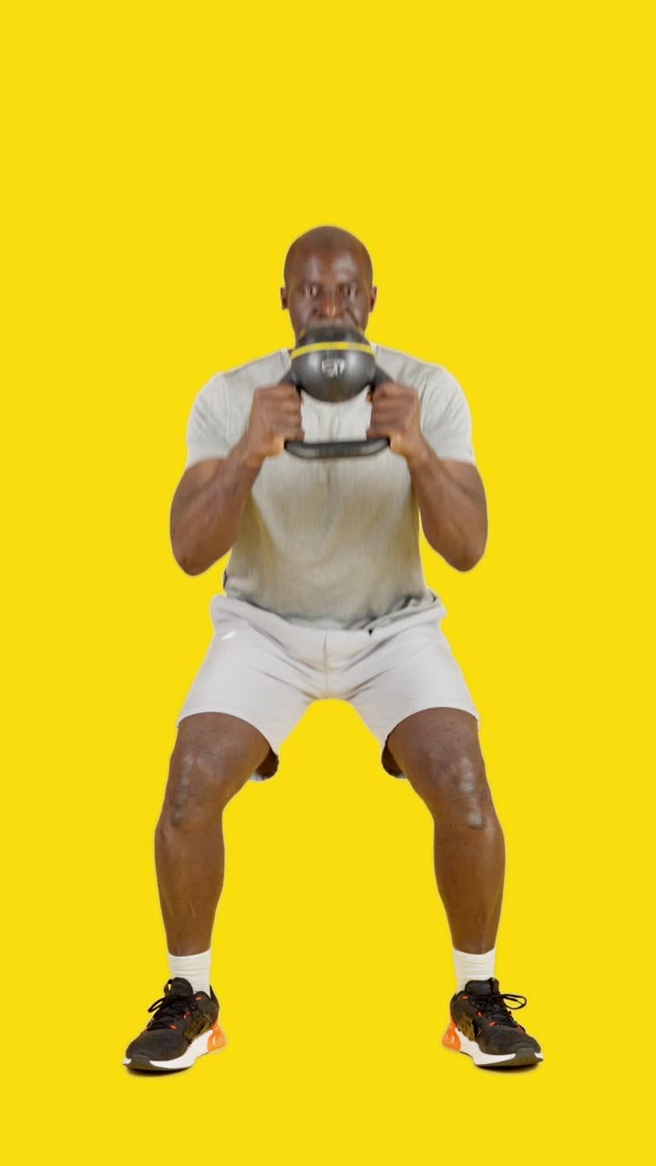 Un uomo che esegue squat con kettlebell su sfondo giallo