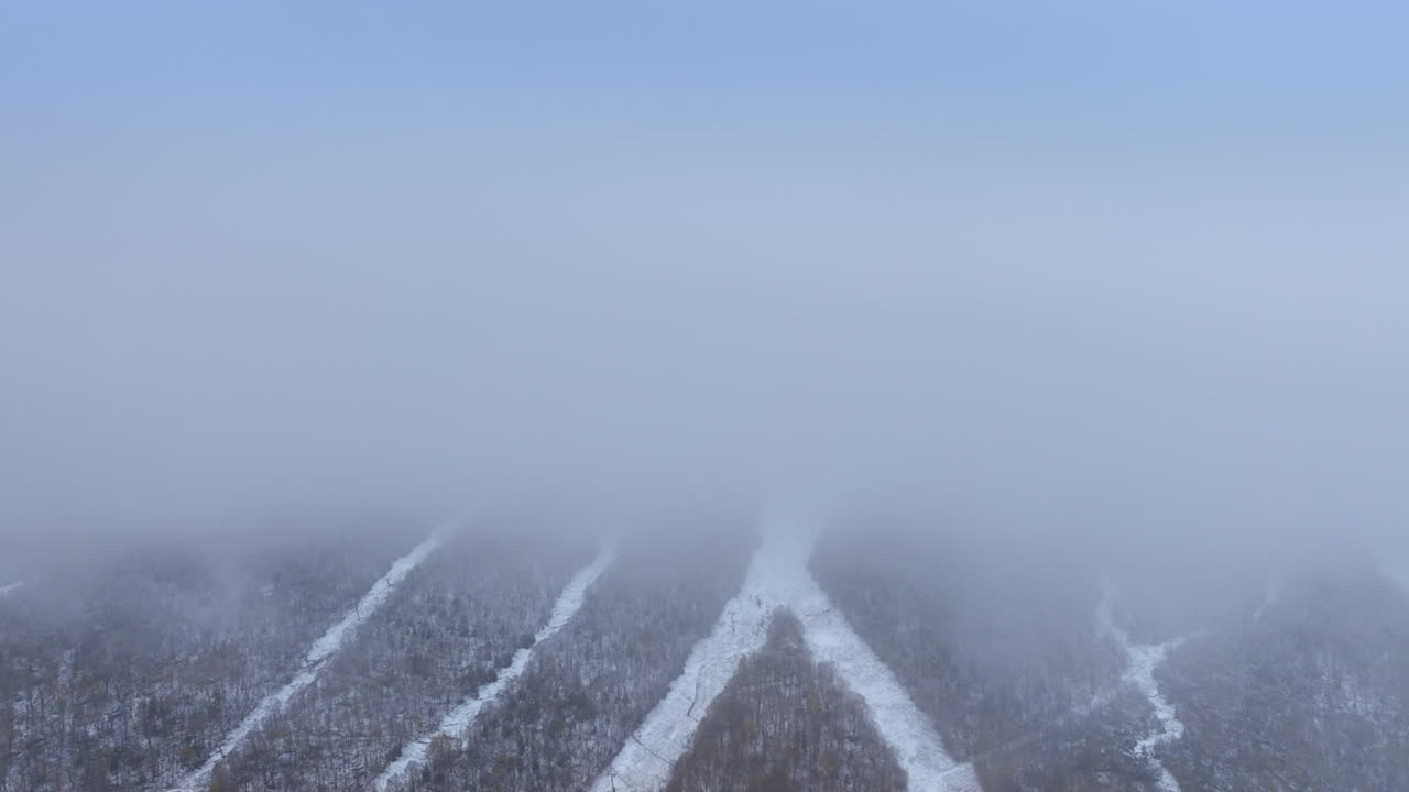 White lines of roads cross the surface of the mountain. Drone footage to the rock top hidden by the thick fog.