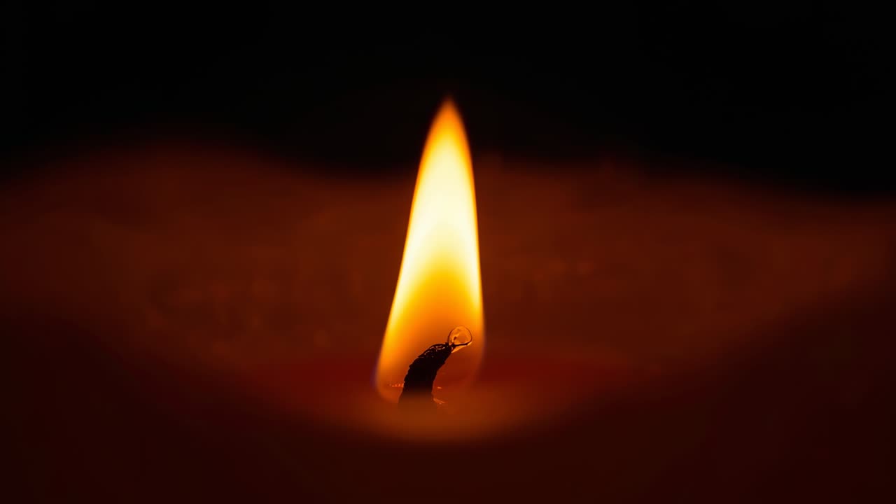 Camera starting filming candle flame pulsing in dark room, showing wax droplet detaching