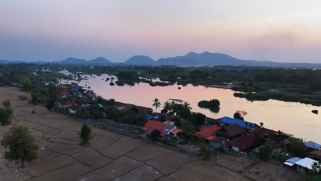 aerial descend sunset view over don det island in southern laos, showing the wide mekong river dotted with islets and the hazy silhouette of the annamite mountains stretching along the horizon