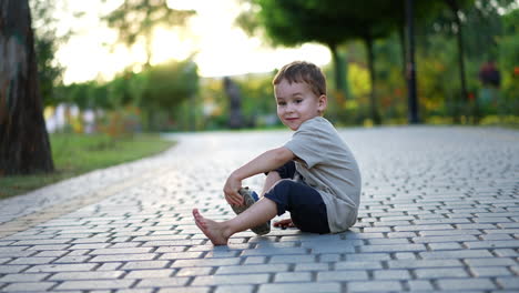 cute little toddler boy sits on the wide paved alley. kid takes off his shoe and throws in the direction of camera. blurred backdrop.