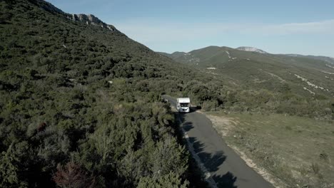 aerial view, white caravan camping van driving through green mountain summer road, panoramic warm skyline