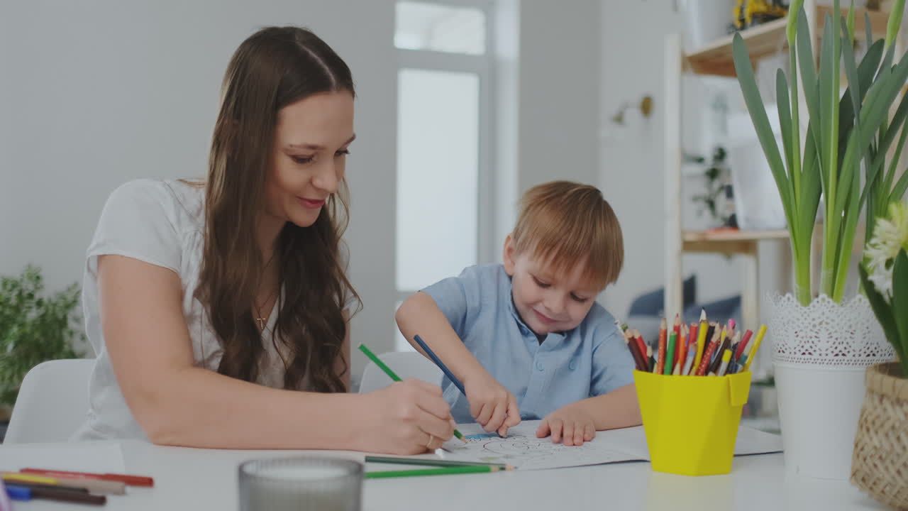 una familia de dos niños y una joven madre sentada en la mesa dibuja en papel con lápices de colores. desarrollo de la creatividad en los niños.