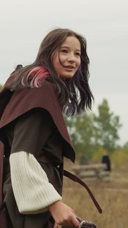 young woman in medieval clothes runs towards wooden houses. female warrior with sword and canvas bag hurries to announce approach of enemy backside view