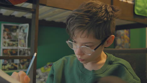 an attractive young boy draws in his sketchbook at his desk in his bedroom