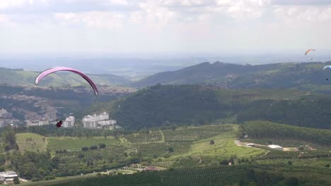 group of para gliders floating through green open valley with mountain range in background