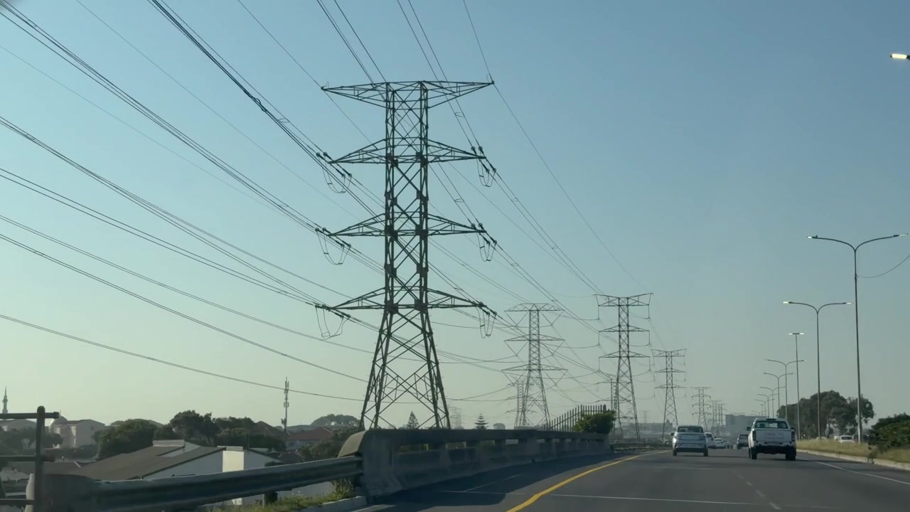 Moving shot of 2 High-Voltage Electricity Pylon and Power Lines Against late afternoon skies.