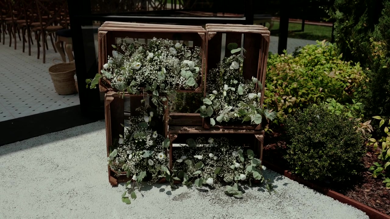 Rustic wooden crates overflowing with delicate white flowers and green foliage, creating a charming decorative arrangement for an outdoor event