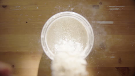 SLOW-MOTION,-TOP-DOWN---Sourdough-starter-is-fed-with-flour-and-water
