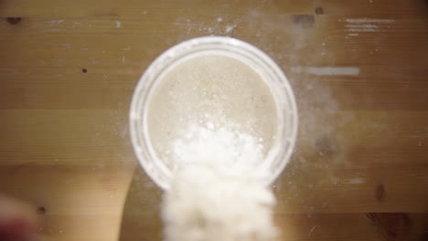 slow motion, top down - sourdough starter is fed with flour and water