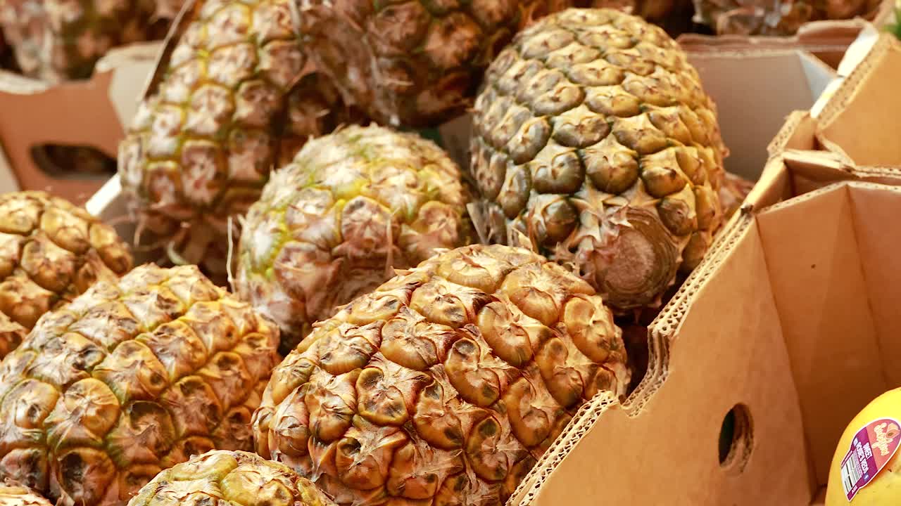 Close-up view of pineapples in a supermarket setting, showcasing natural textures and vibrant colors under bright lighting