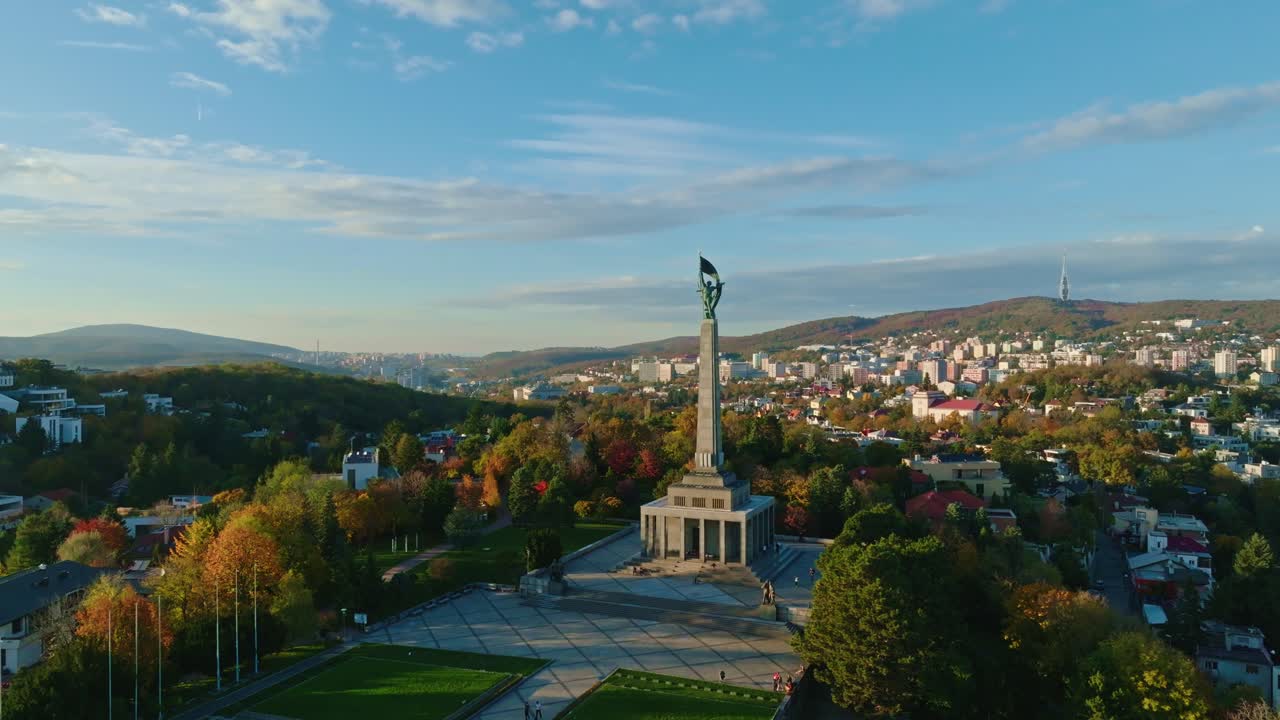 Drone view of Slavin War Memorial in Bratislava, Slovakia, surrounded by autumn foliage and panoramic cityscape under a clear blue sky