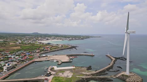 Stunning-drone-view-of-Woljeong-Beach's-pristine-shores,-a-tranquil-oasis-on-beautiful-Jeju-Island,-with-a-unique-view-of-Wind-Turbines-in-right-on-the-waters-edge