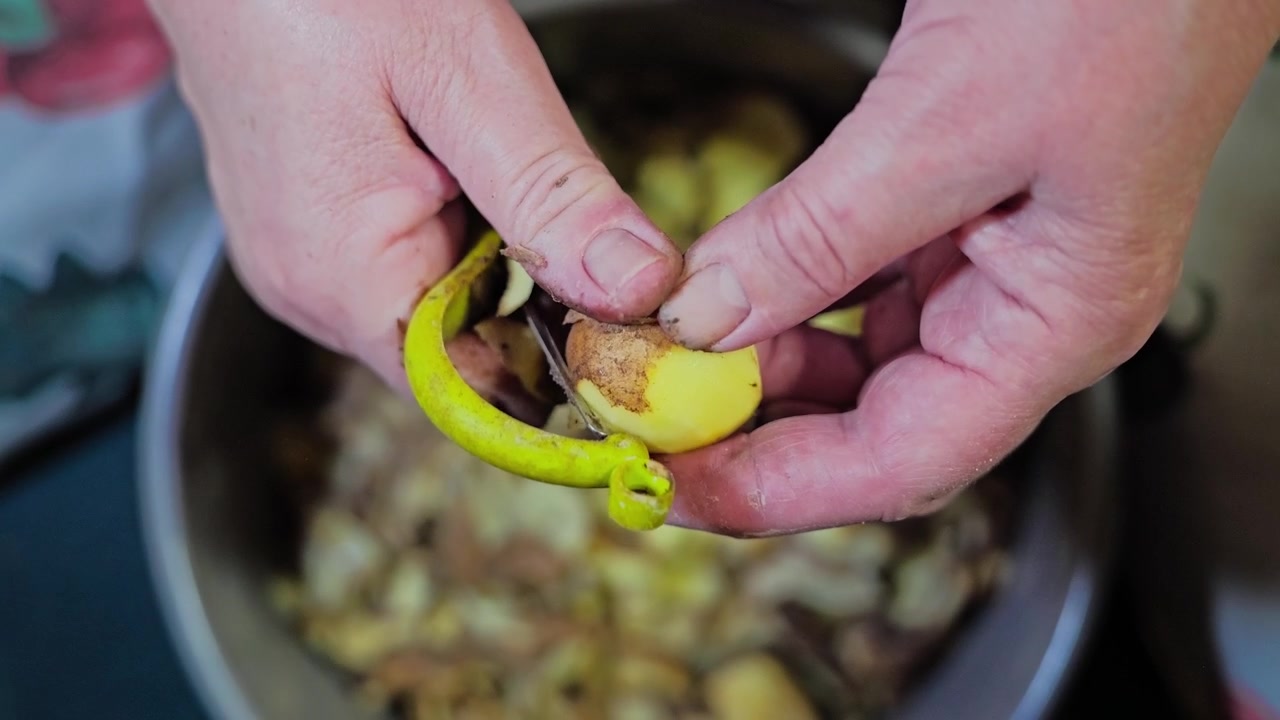 Mani che pelano una patata fresca con un coltello durante la preparazione di cibo fatto in casa, al rallentatore