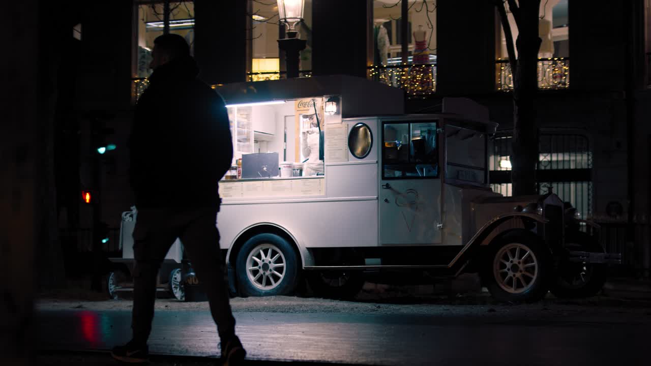 Silhouet van een man die 's nachts over straat loopt met een foodtruck.