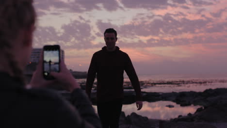 Pareja-Joven-Divirtiéndose-Tomando-Fotos-En-La-Playa-Hombre-Posando-Con-Los-Brazos-Levantados-Feliz-Alegre