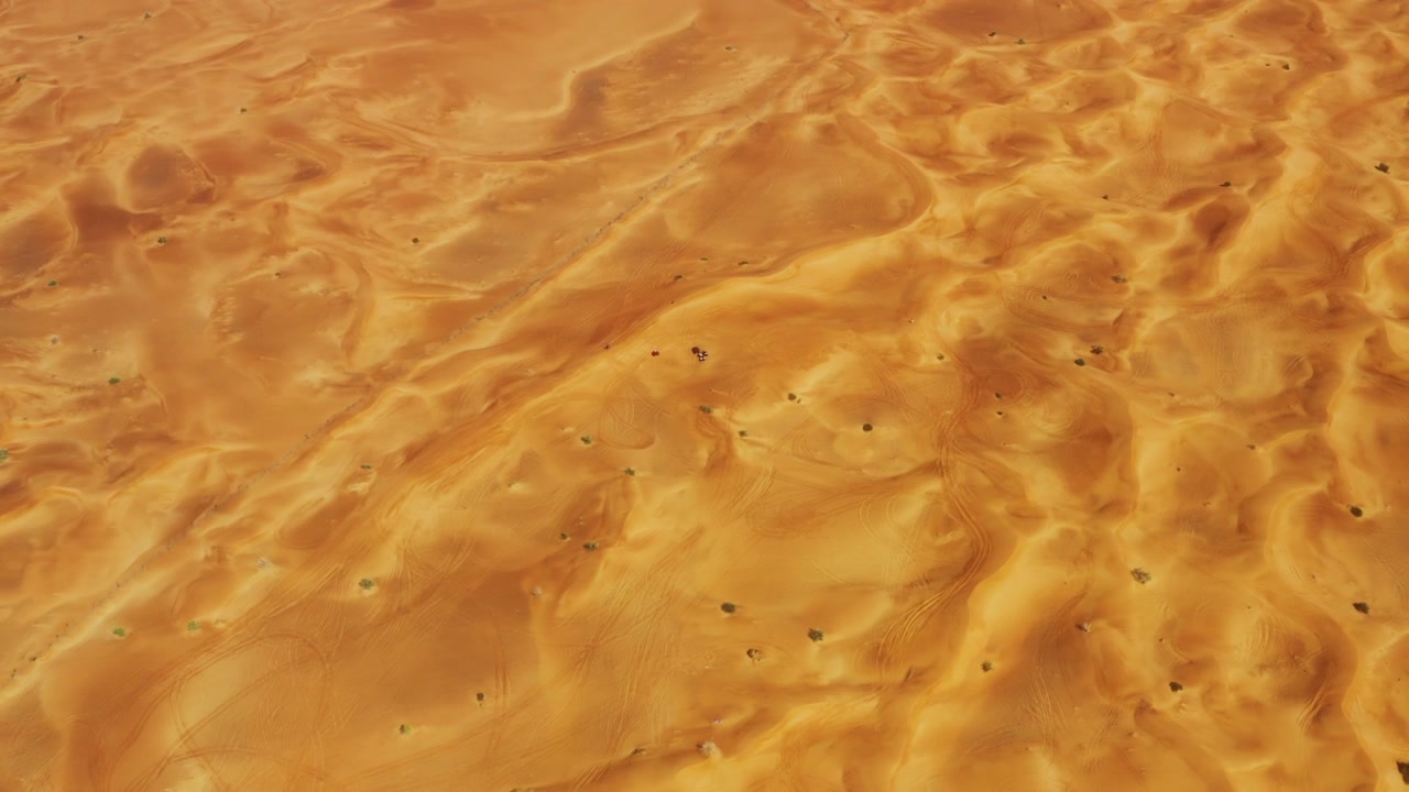Vista aérea de drone de alta altitude movendo-se lentamente sobre as dunas do deserto de Dubai, revelando curvas naturais abstratas, cristas e padrões na areia