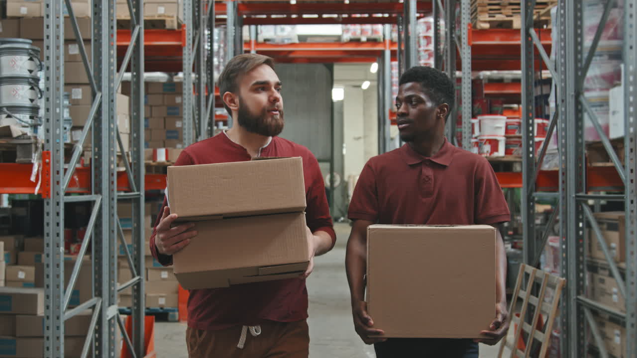 Coworkers Talking and Carrying Boxes in Warehouse