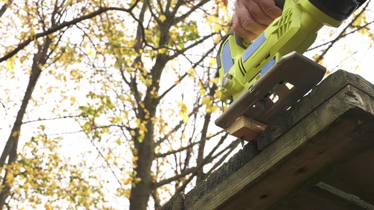 A person is using a jig saw to cut wood in a backyard setting. Sunlight filters through trees, creating a warm and inviting atmosphere for this woodworking project