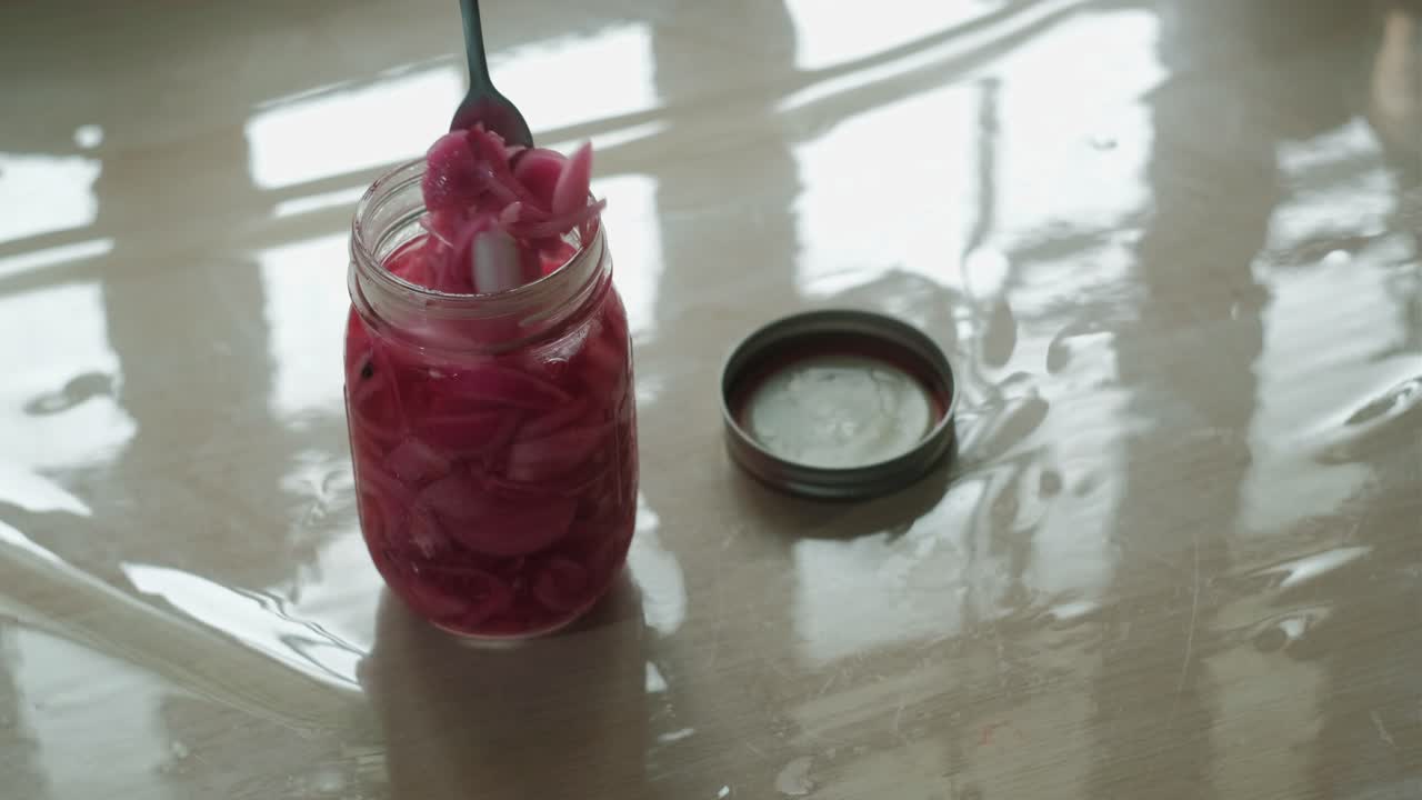 Fork scooping pickled onions condiment out of a mason jar. static shot
