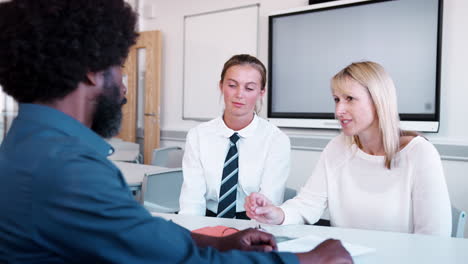 mother and teenage daughter having discussion with male teacher at high school parents evening