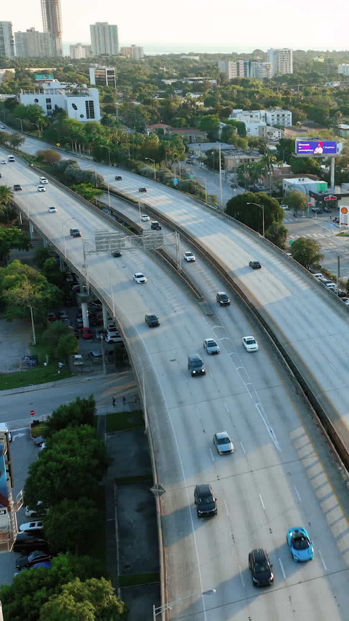 Miami, Florida, USA - January 05, 2024: Aerial flight over Interstate 95 with heavy traffic. Cars in city center at sunset. Downtown with small houses and green trees. Vertical video