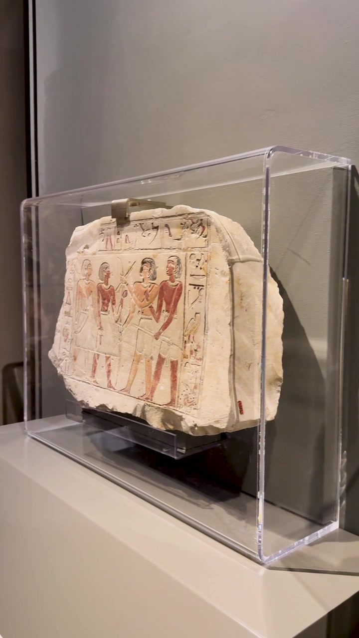 La telecamera scorre su antichi rilievi in pietra egizi e geroglifici protetti in teche di vetro museali.