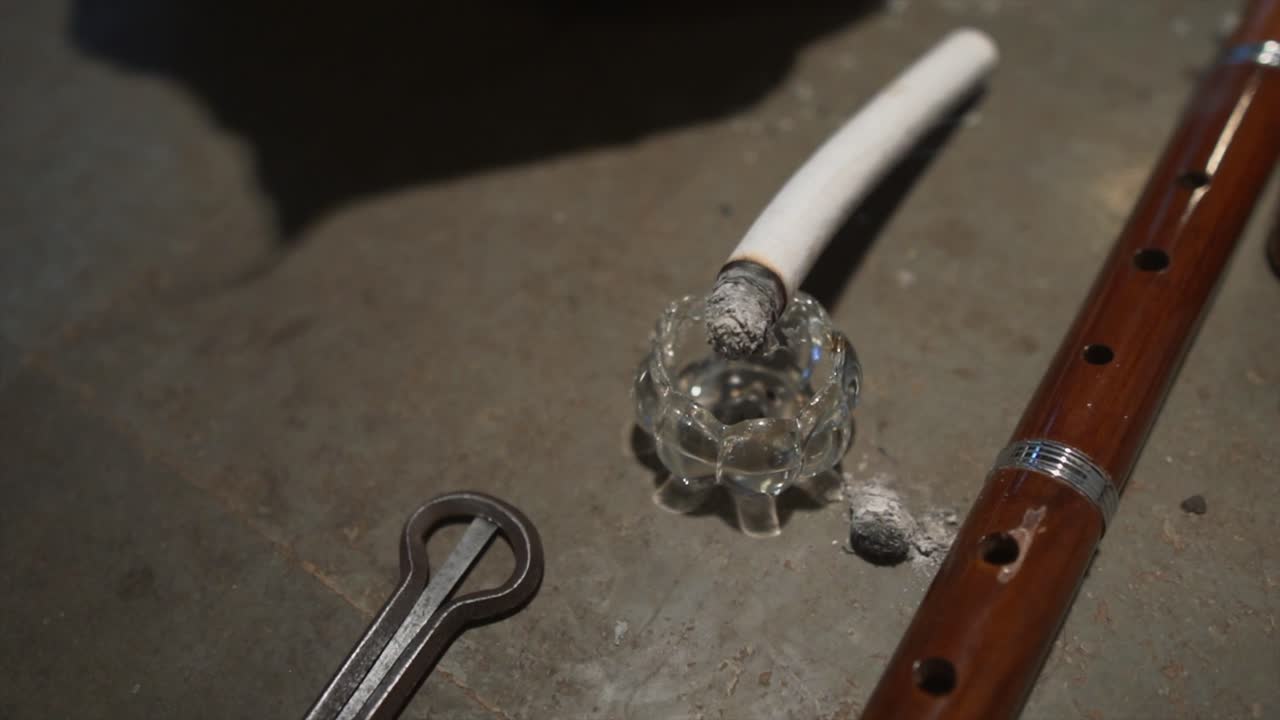 cigarrillo ardiendo lentamente en un cenicero diminuto, junto a una flauta y un arpa diminuta