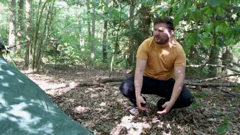 man pitches a tent at a campsite in the woods but fails and drops the hook and string