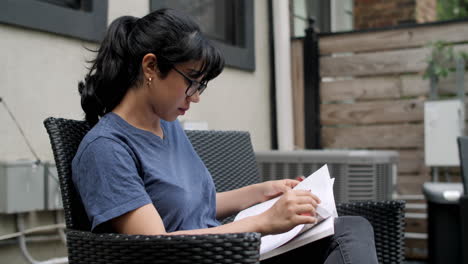 una joven latina sentada en un patio trasero estudiando un libro de texto