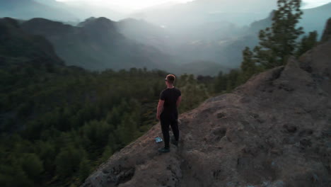 empowering aerial shot of confident guy standing on the edge of a cliff in gran canaria during the sunset